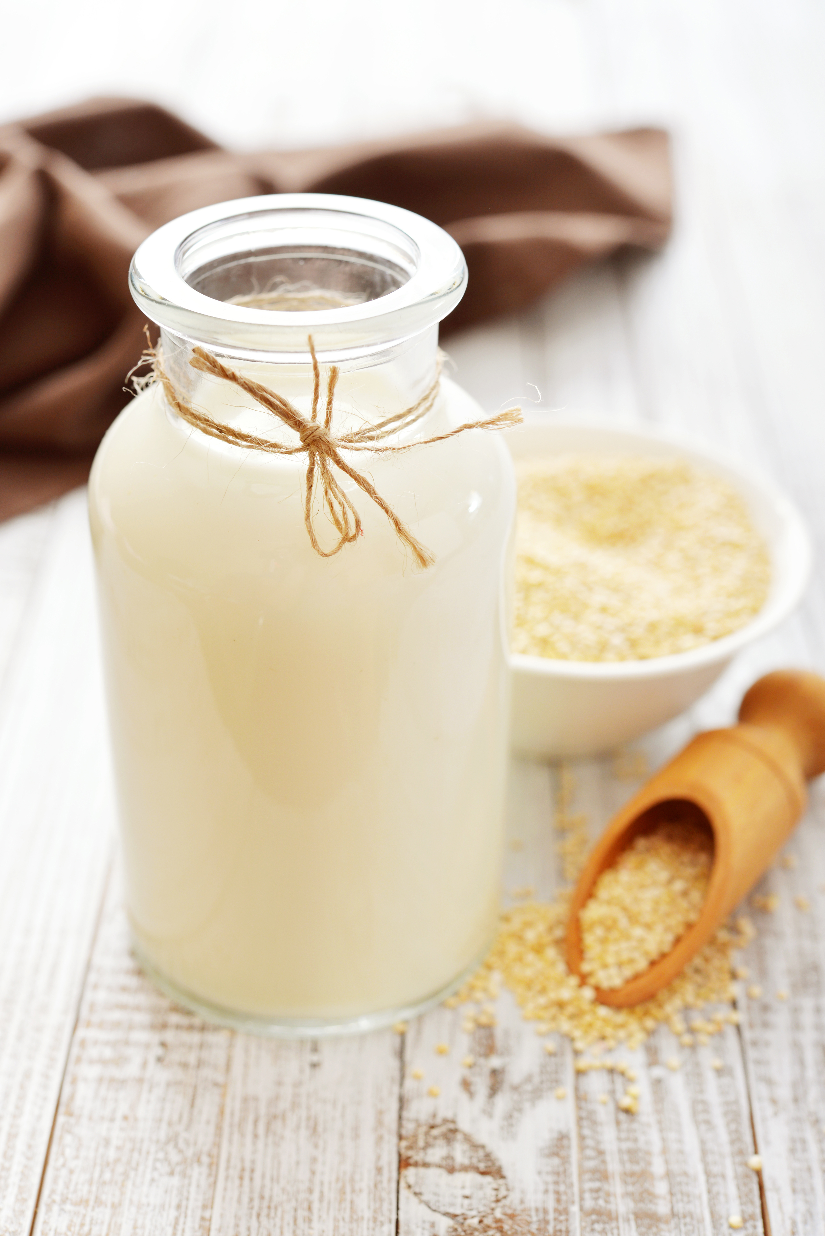Växtdryck av quinoa i en glasflaska med vit quinoa på ett bord