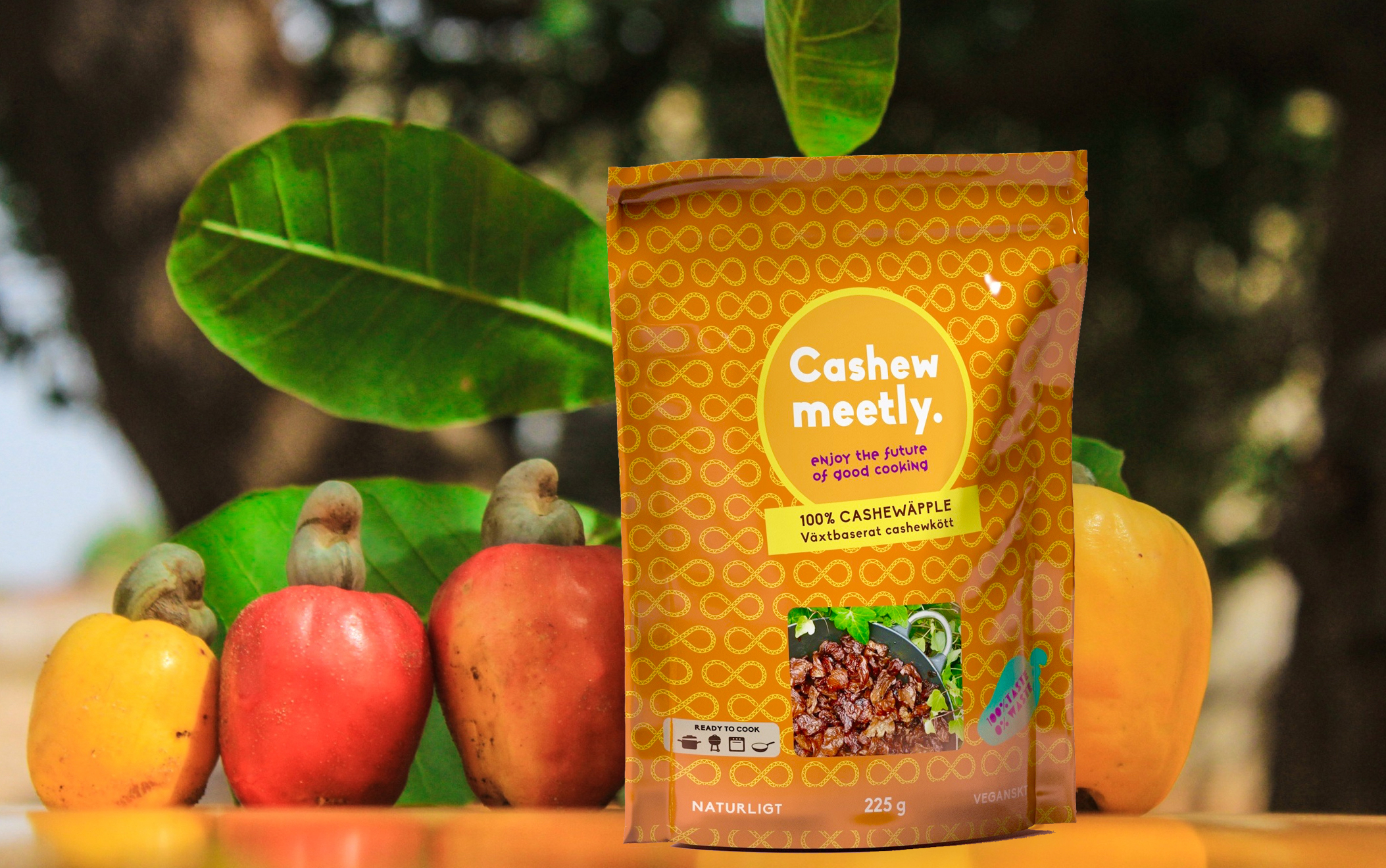 Foto: Axfood/Cashewmeetly Cashewmeetly i förpackning med cashewäpplen och grönska i bakgrunden.