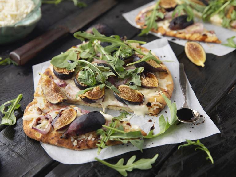 Vegansk pizza med fikon och ruccola på ett mörkt bord