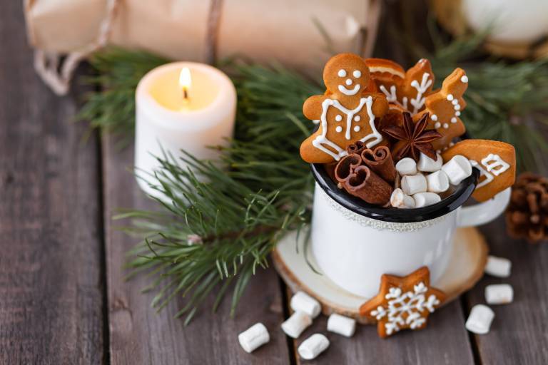 Hot winter drink in a white mug: cozy home composition with homemade gingerbread cookies, tree branch. Wooden background, christmas lights and candles