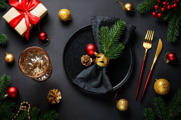 Christmas table setting with black plate, wine glass, cutlery and holidays decorations.