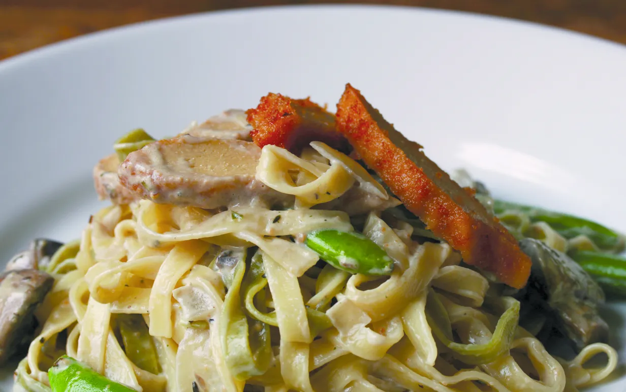 Pasta med sojakyckling och sockerärtor på en vit tallrik
