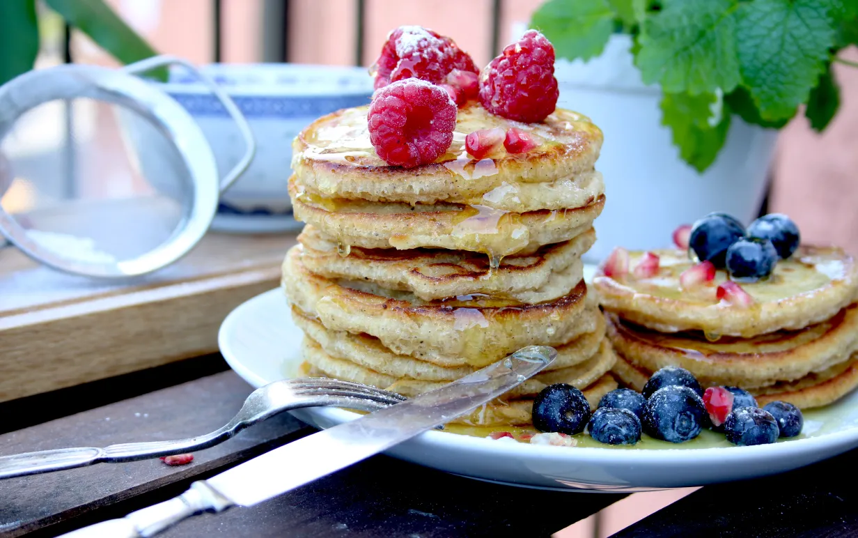 Veganska amerikanska pannkakor på en vit tallrik toppade med färska blåbär och hallon.