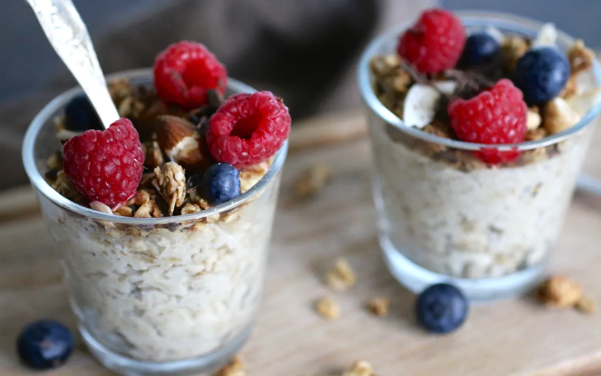 Två glas med overnight oats toppade med hallon och blåbär.