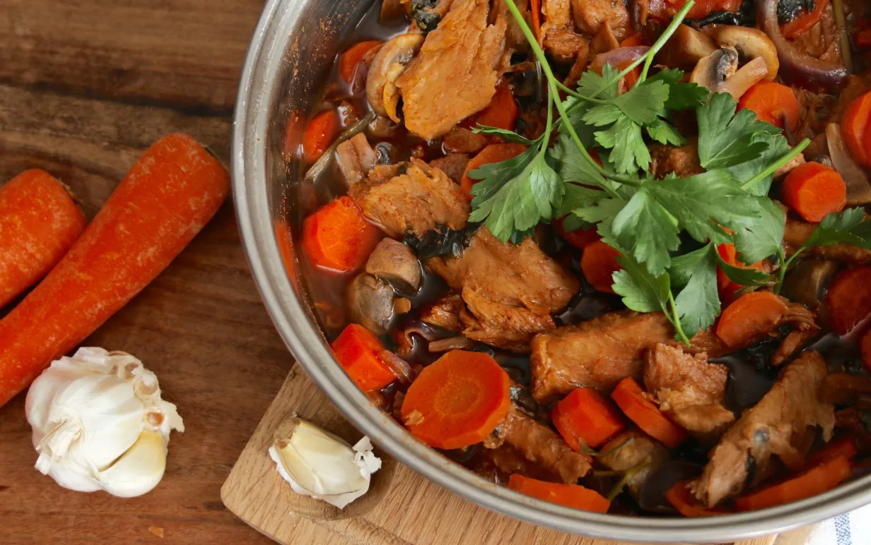 en tallrik med mustig viltgryta på ett bord, bredvid ligger några morötter och en vitlök