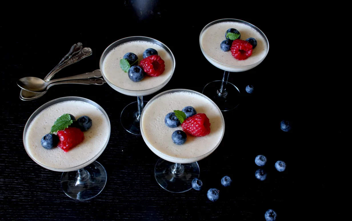 Fyra glas med pannacotta, dekorerad med hallon och blåbär.