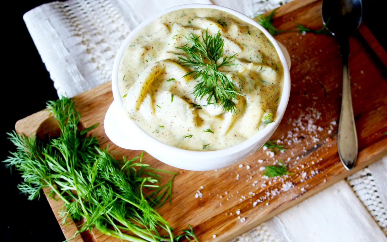 Auberginesill i senapssås i en skål på en skärbräda, garnerad med dill.