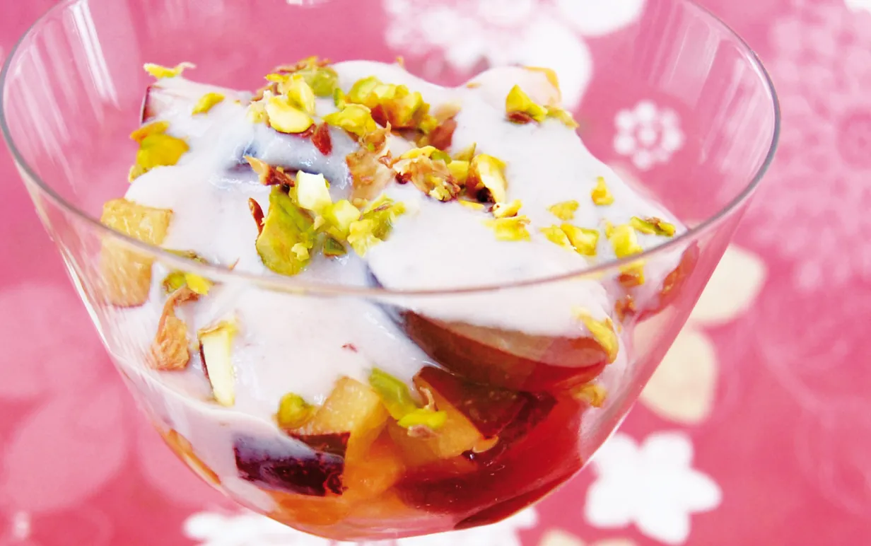 Fruktsallad med pistagenötter och vaniljyoghurt i en glasbägare.