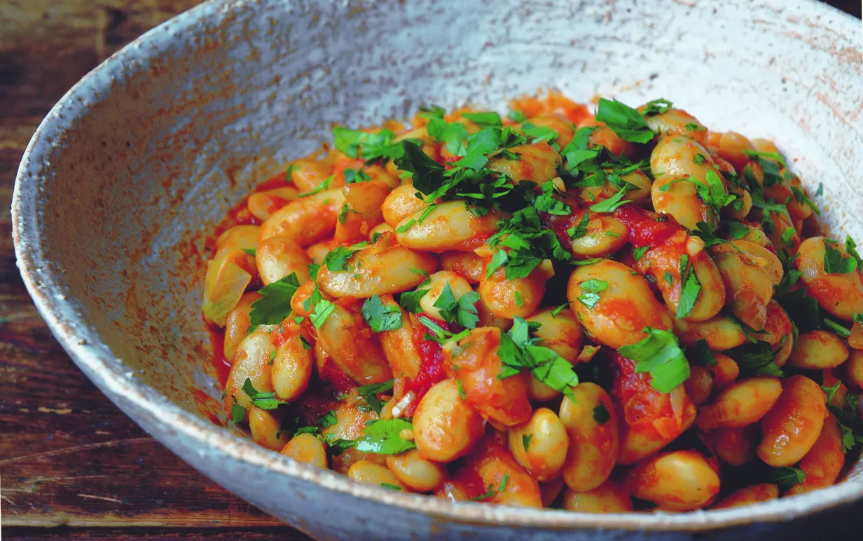 Ugnsbakade bönor i en skål, toppade med persilja.