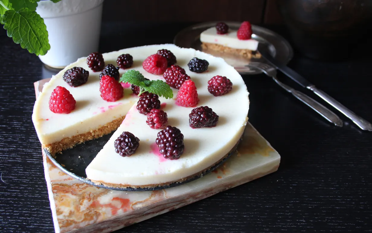 Cheesecake med citronfyllning dekorerad med hallon och björnbär på ett mörkt bord