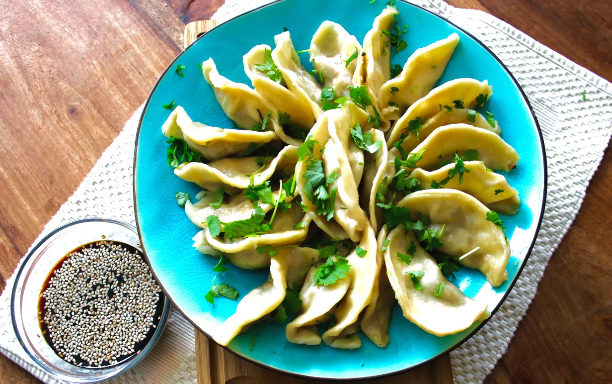 Veganska dumplings på ett blått fat. Bredvid står en skål med japansk soya.