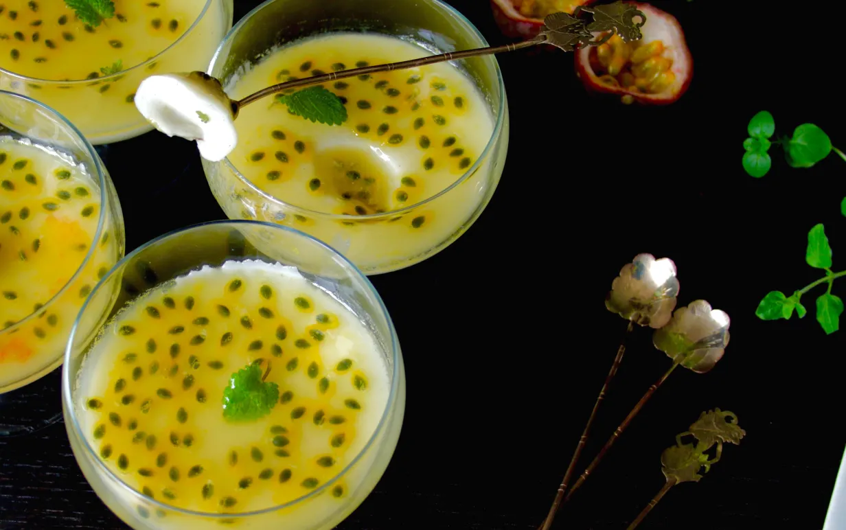 Fyra bägare med pannacotta med passionsfrukt på ett mörkt bord.