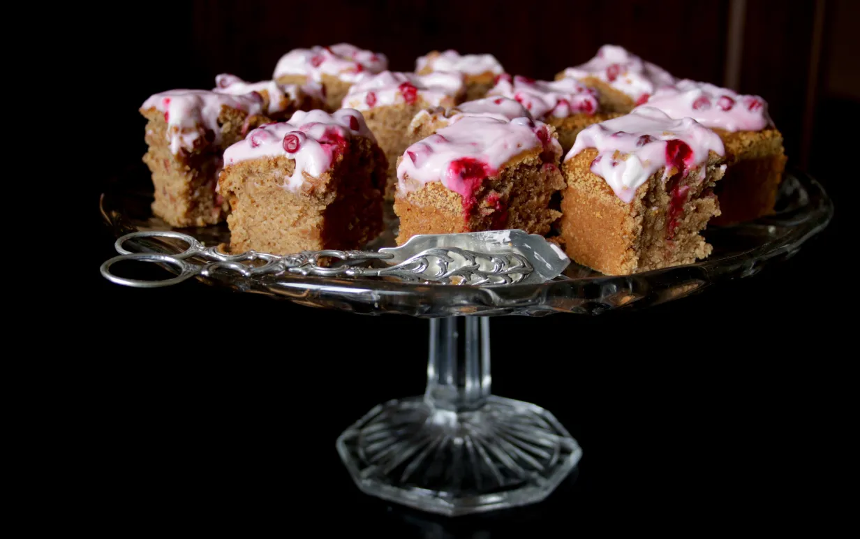 Bitar av mjuk pepparkaka med lingonfrosting på ett kakafat av glas.