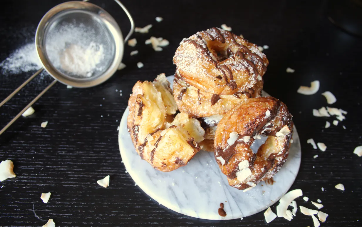 Cronuts med choklad och kokosflarn på ett vitt fat på ett mörkt bord