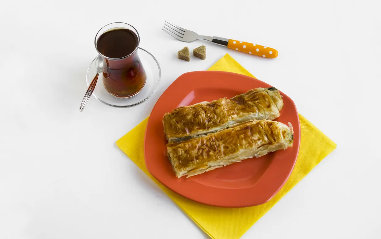 vegan börek på en orange tallrik, bredvid står ett glas med te