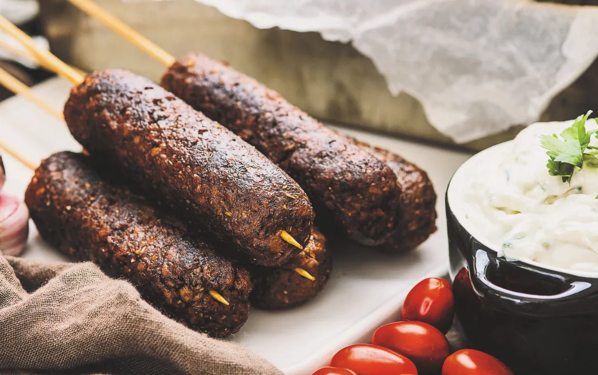 kebabspett på en vit skärbräda, bredvid spetten står en skål med tzatziki