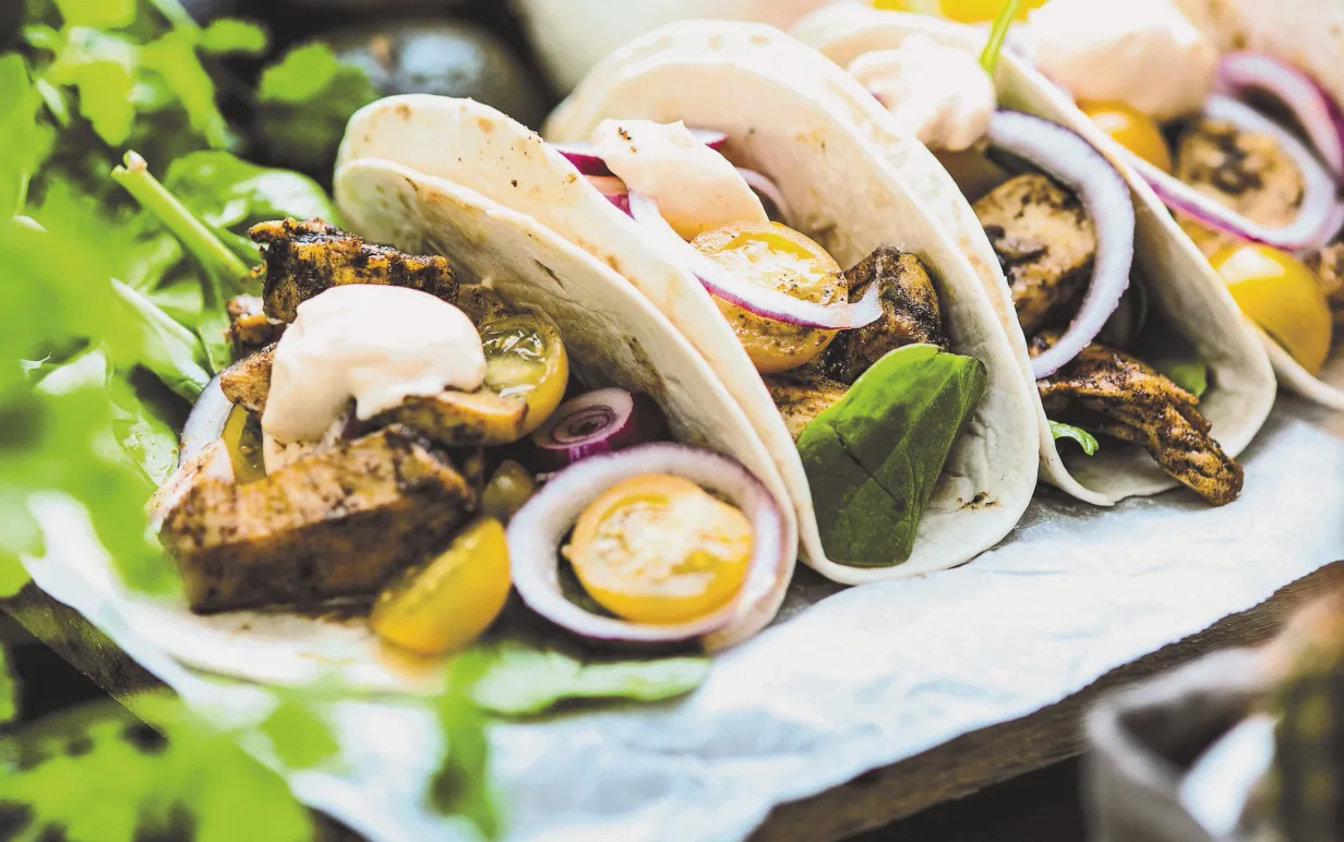 Fyra stycken tacos ligger på en vit handduk, i förgrunden syns gröna blad