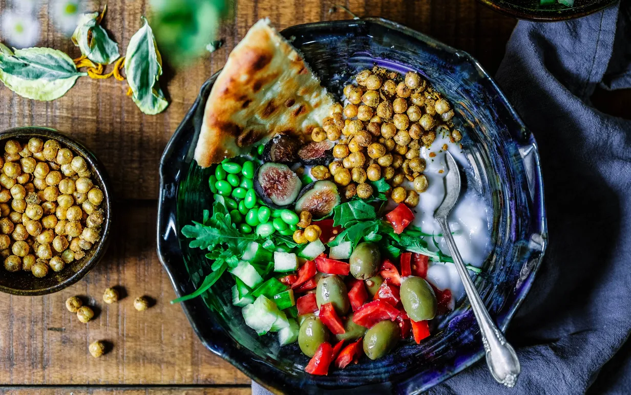 skål med kikärtor, grönsaker och sås på ett bord