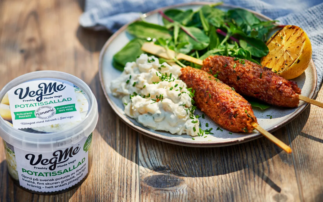 Förpackning av potatissallad intill en tallrik med potatissallad med vegansk spett