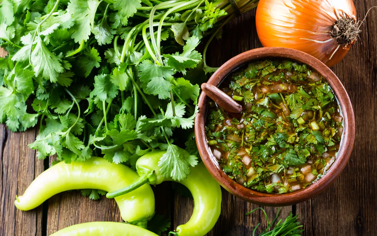 En skål med pebre tillsammans med lök, chili och koriander på ett bord