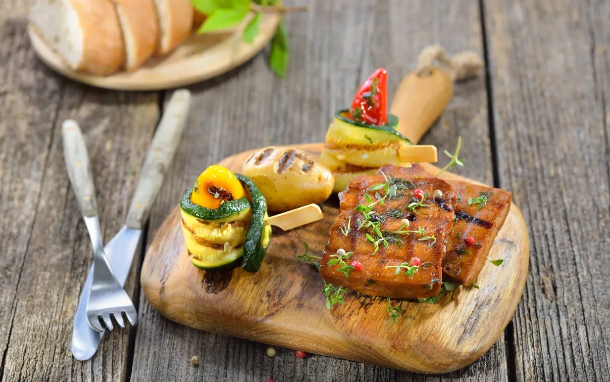 Vegansk seitan på en träbräda intill grönsaker