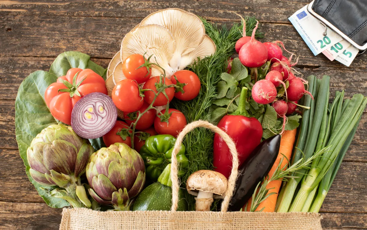 Grönsaker i en korg intill en plånbok med sedlar