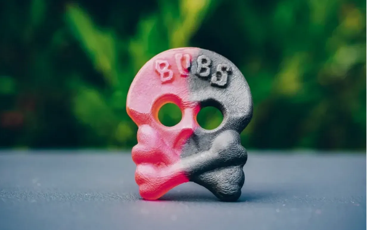 Hallonlakritsskallen, röd ena halvan svart andra halvan, står BUBS i pannan, står på ett svart golv mot en grön bakgrund