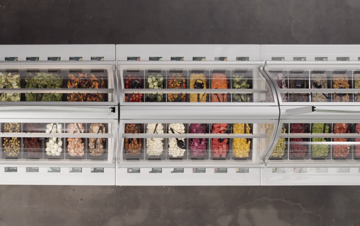 Salladsbar med många olika, färgglada alternativ, fotad ovanifrån mot mörkgrått golv.