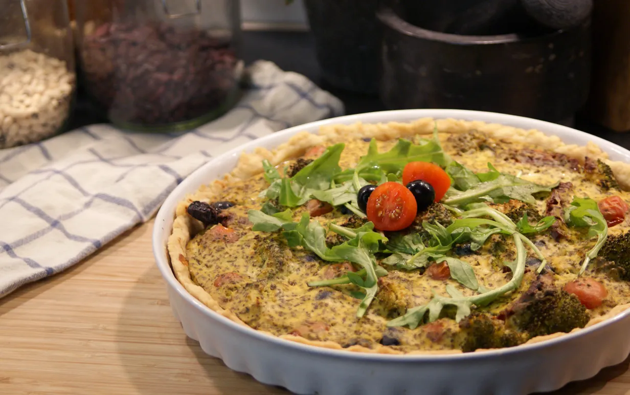 Nygräddad matpaj i vit pajform, ståendes på en skärbräda av trä. Bredvid ligger en rutig kökshandhud.