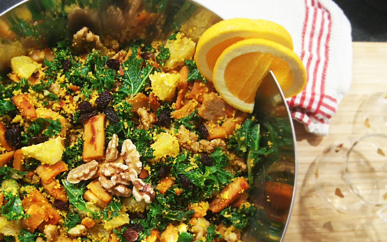 Grönkålssallad med saffranscouscous, apelsin, valnötter och russin i en skål.