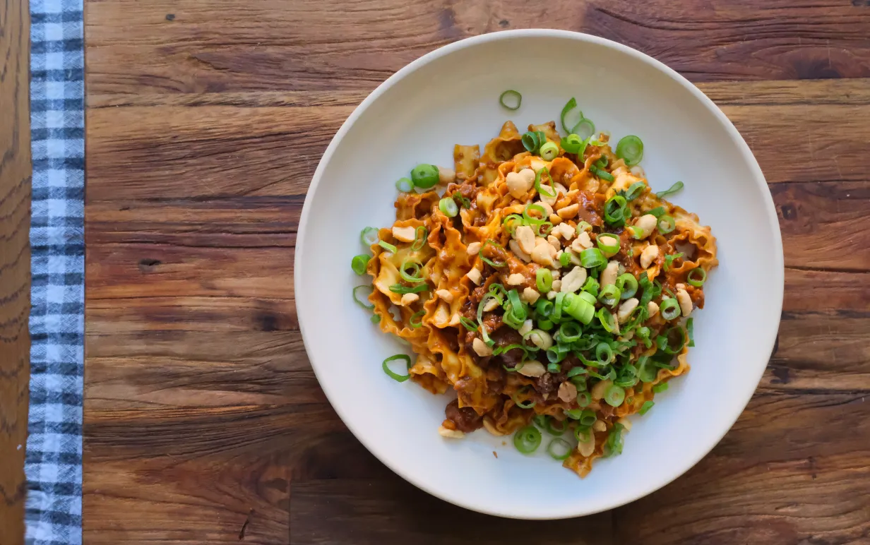 Veganska nudlar uppdukad på en vitt tallrik på ett träbord.