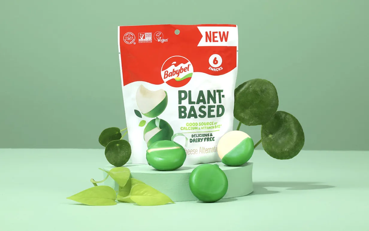 Växtbaserade Babybel-ostar i grönt vax framför produktpåsen mot en grön bakgrund.