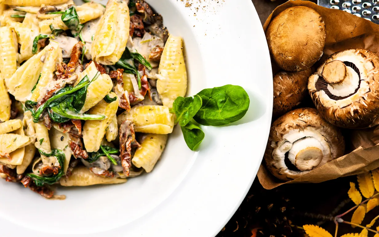 En vit djuptallrik med krämig pasta med svamp och basilika.