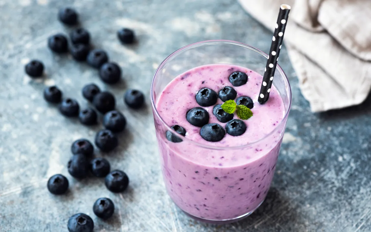 Blåbärssmoothie i ett glas med sugrör i papp med blåbär som garnering.