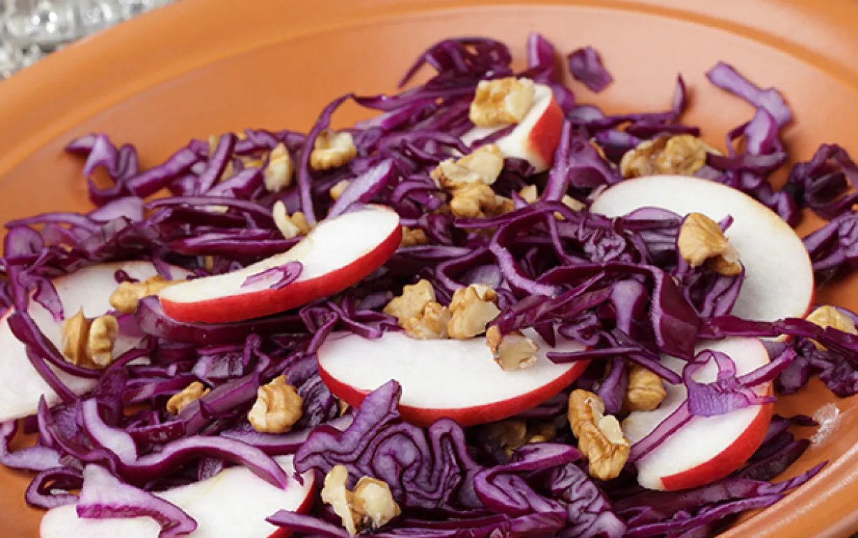 Rödkålssallad med äppelskivor och valnötter i ett keramikfat.