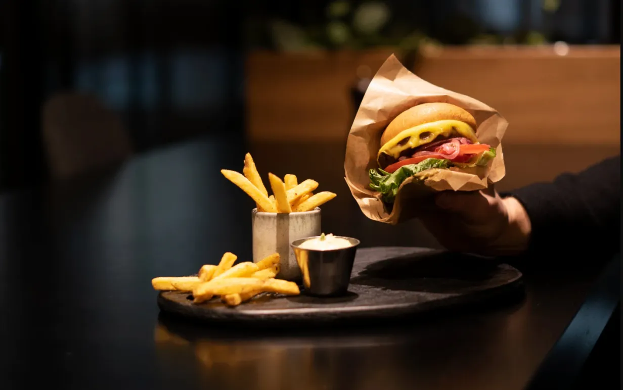 en hand som håller i en vegoburgare med pommes och dip på ett bord i en mörk restaurangmiljö