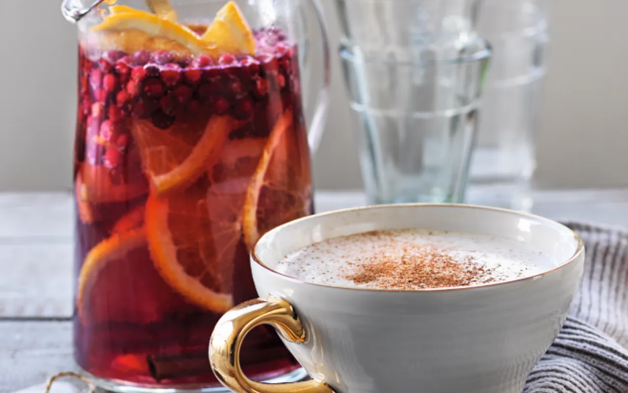 Toddy i en vit mugg med guldhandtag bredvid en karaff med sangria.