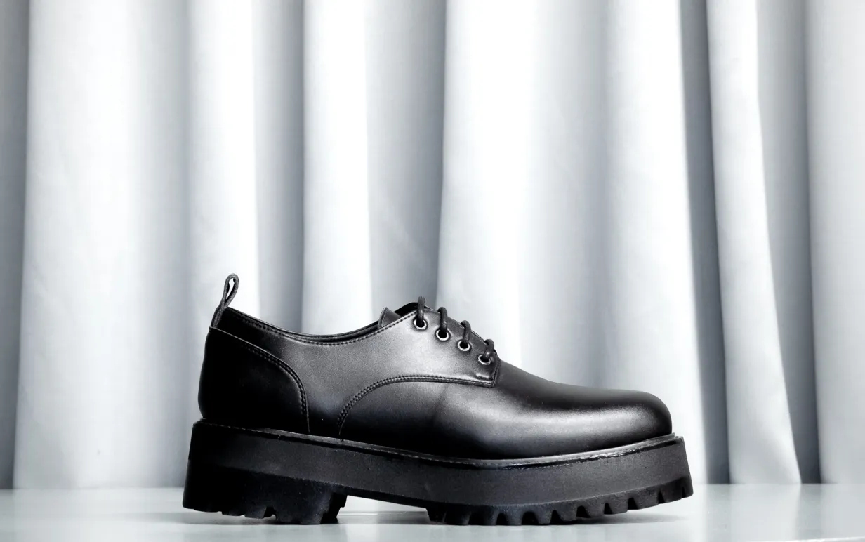 Svart veganska låg känga mot ett ljusgrått draperi