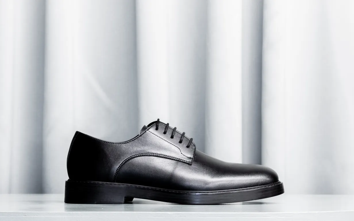 Svart veganska låg känga mot ett ljusgrått draperi