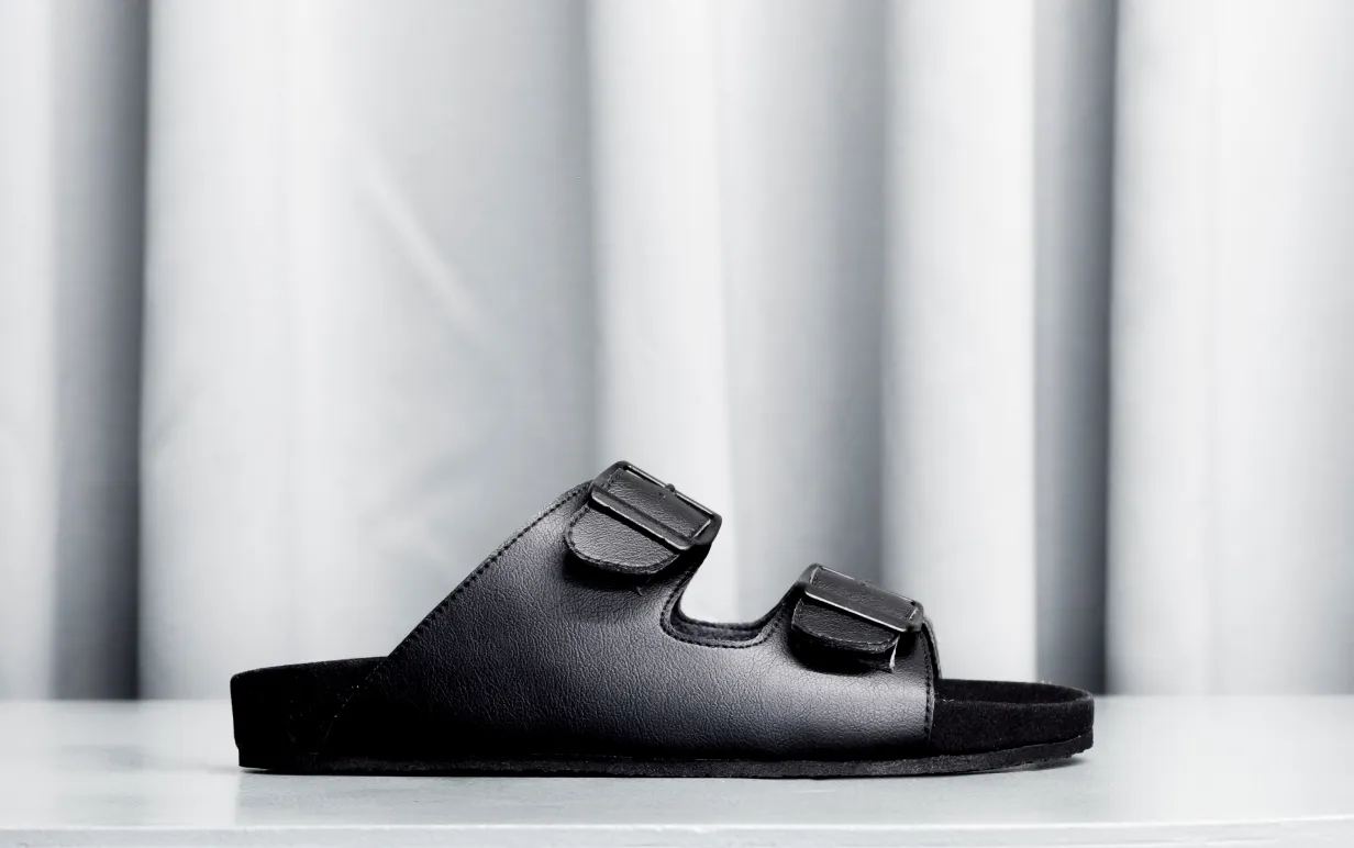 Svart veganska toffla mot ett ljusgrått draperi