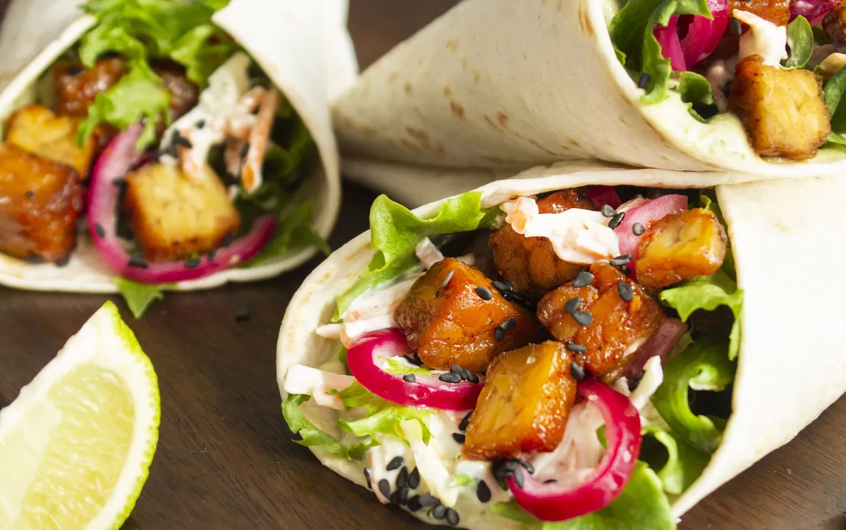 tre veganska wraps uppstaplade på en skärbräda i trä