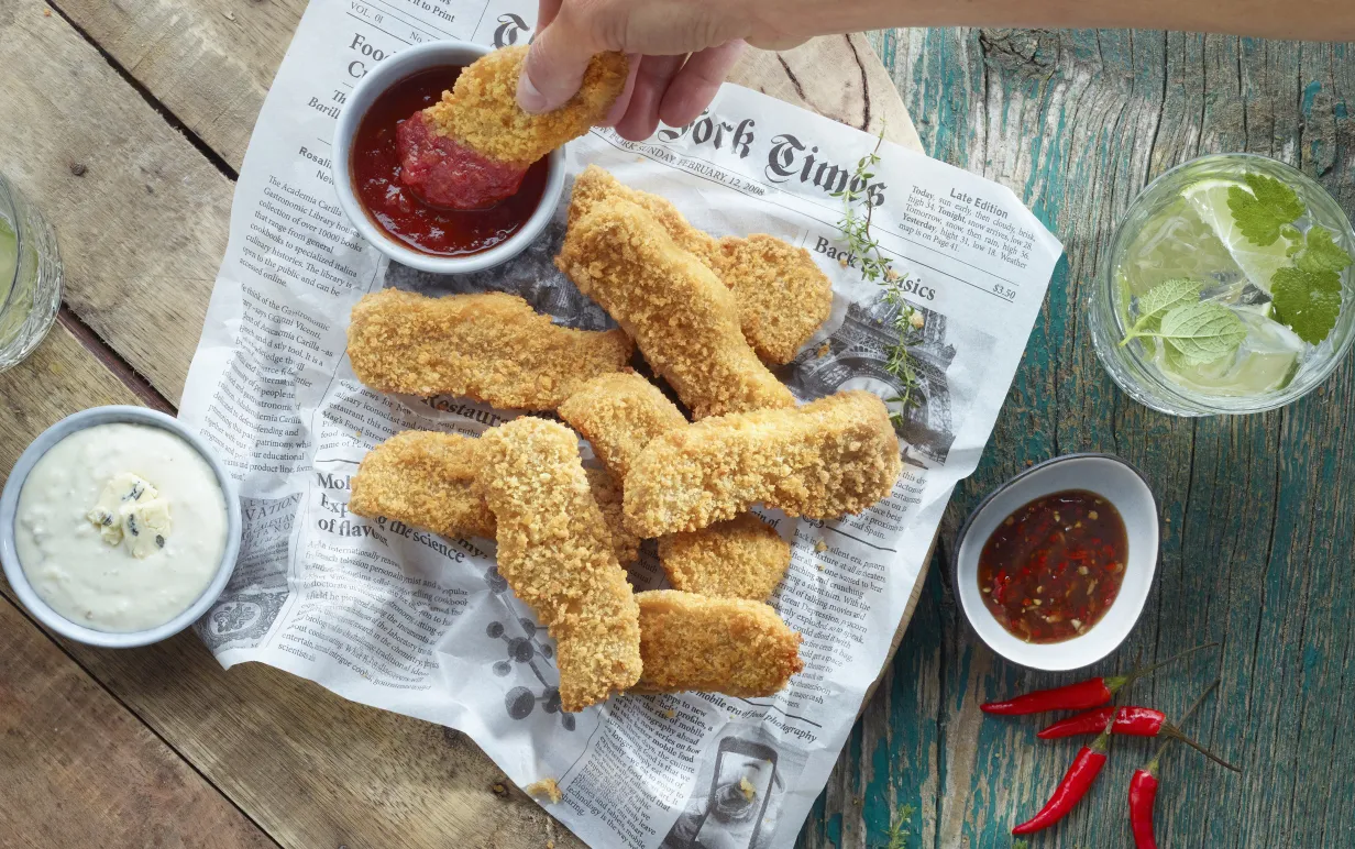 Veganska chicken fingers på ett tidningspapper med massa dippar runt om.