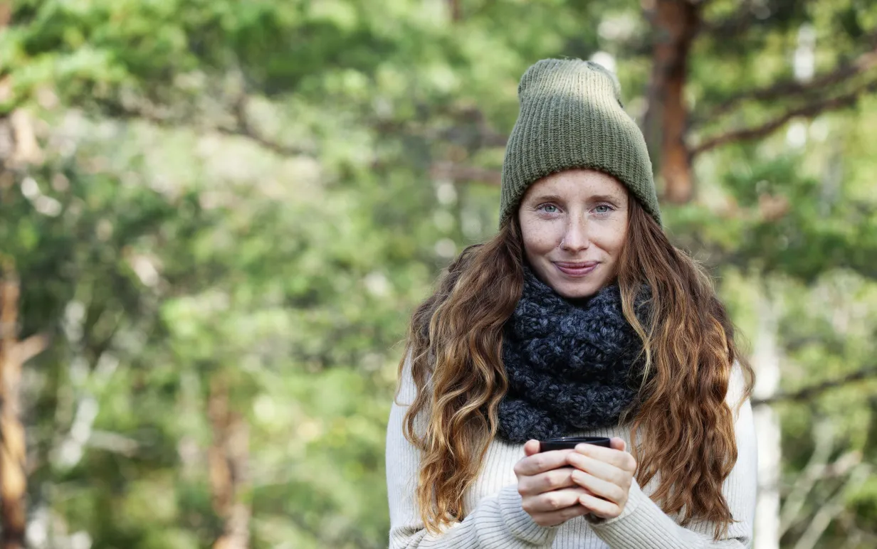 Kvinna ute i naturen med en kopp i sina händer.