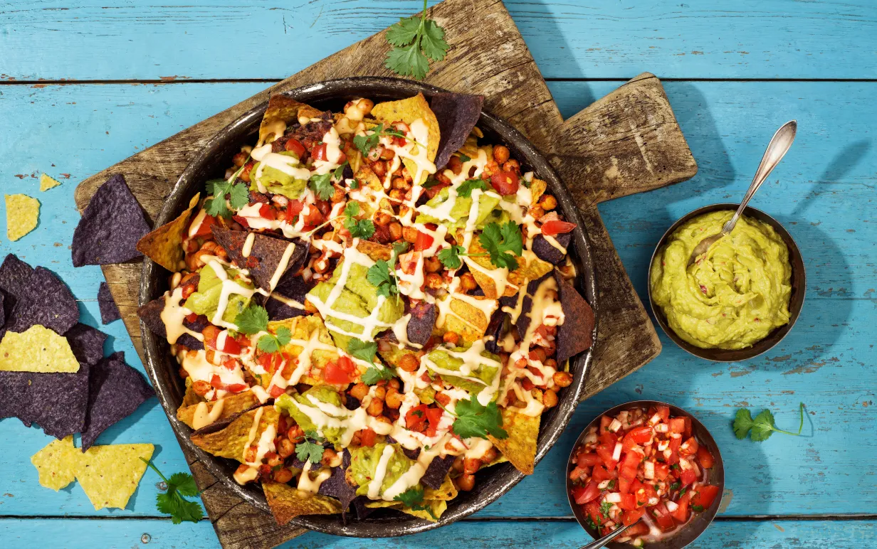 En tallrik med nachos på en skärbräda i trä som står på ett turkost träbord