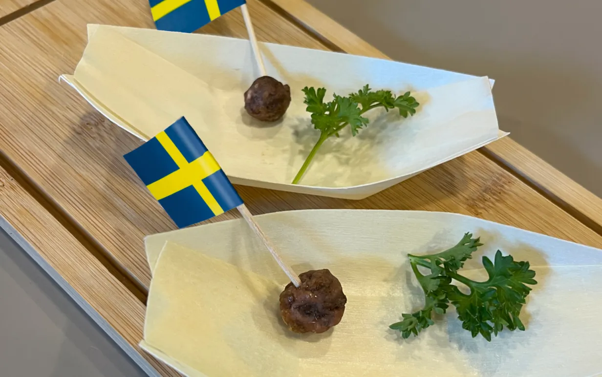 Två odlade köttbullar på vita fat med små svenska flaggor i och kvistar med persilja på sidan om