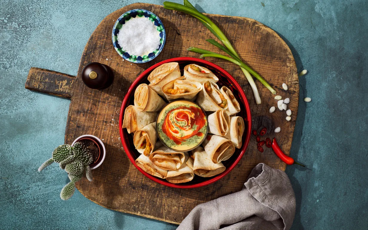 En tallrik med nachos på en skärbräda i trä som står på ett bråblåt bord