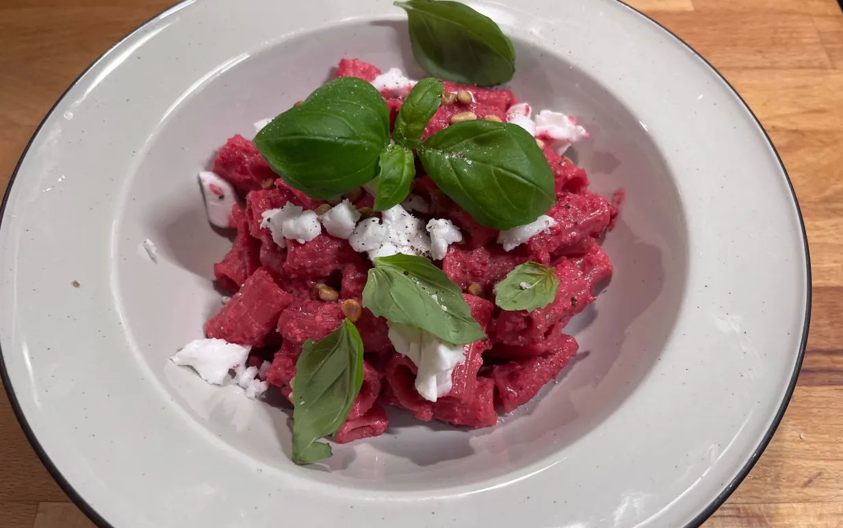 En djuptallrik med rödbetspasta, dekorerad med vegansk feta, pinjenötter och basilika
