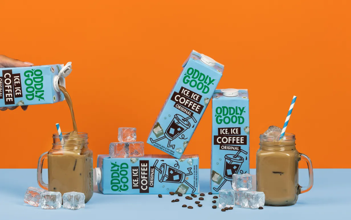 Förpackningar med växtdryck och glas med iskaffe mot en orange bakgrund.