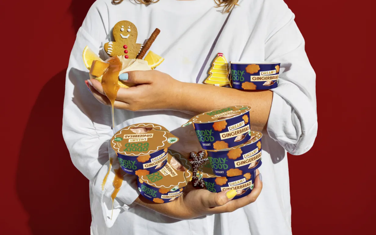 Person i vit tshirt mot en röd bakgrund som håller i flera burkar med packeterad dessert