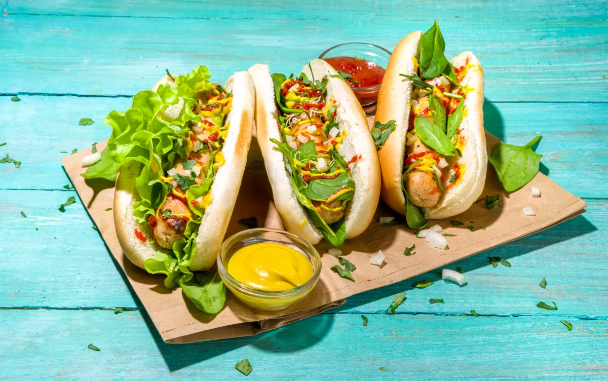 Tre veganska korv med bröd på ett bakplåtspapper på ett turkost träbord